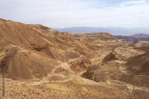 The small curve path among sandstone hills with rocky slopes and the blue sky with white clouds