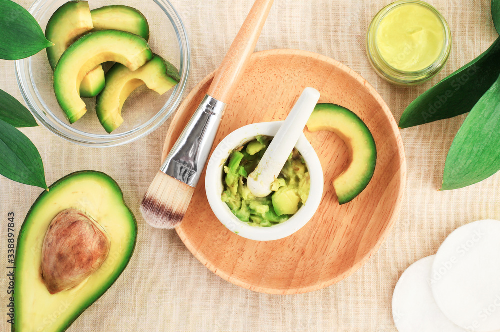 Making skincare treatment product with fresh ripe green avocado, mixed in mortar crushing food slices, wooden bowl cosmetic brush facial mask healthy beauty treatment, top view overhead background. Making skincare treatment product with fresh ripe green avocado, mixed in mortar crushing food slices, wooden bowl cosmetic brush facial mask healthy beauty treatment, top view overhead background.