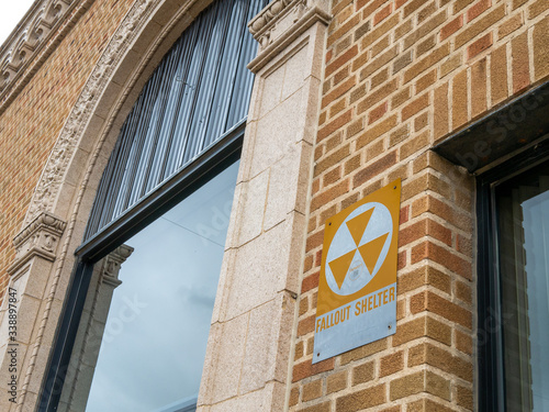 Old vintage fallout shelter sign on a brick exterior wall between a door and a large decorative window. photo