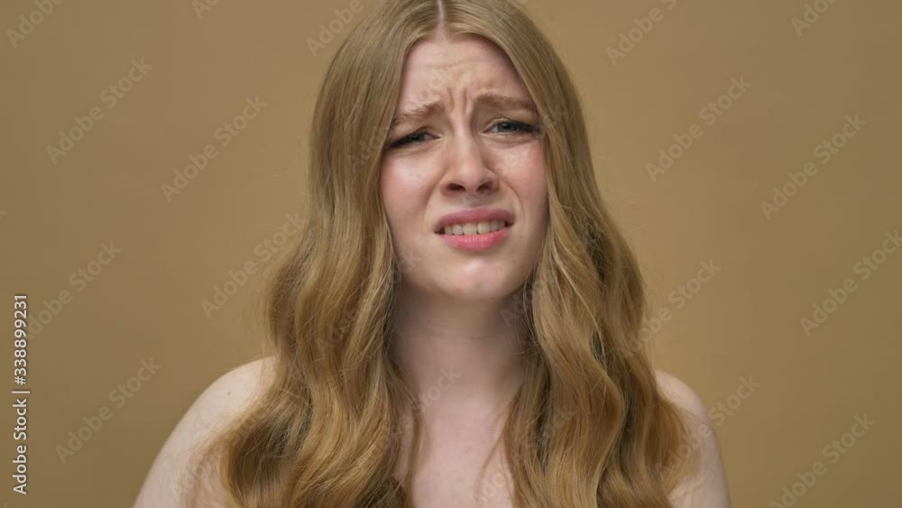 A displeased young half-naked woman with long hair is showing a thumb down gesture isolated over beige background A displeased young half-naked woman with long hair is showing a thumb down gesture isolated over beige background