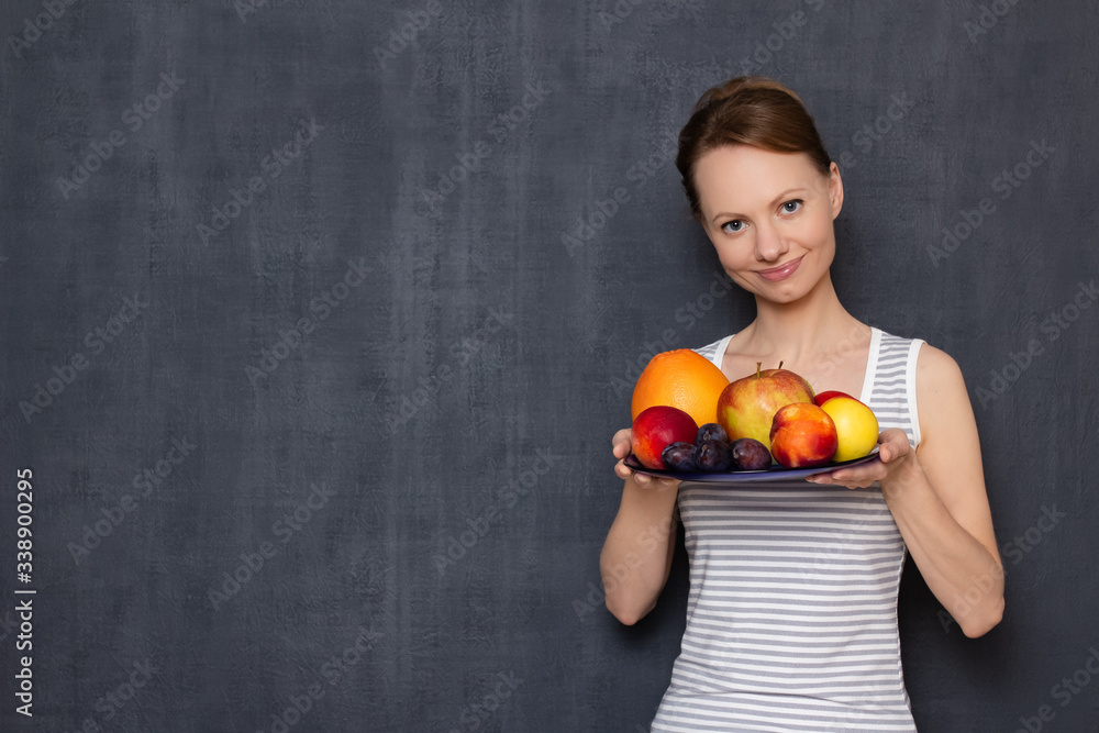 Portrait of happy young woman holding plate of ripe fresh fruits Portrait of happy young woman holding plate of ripe fresh fruits