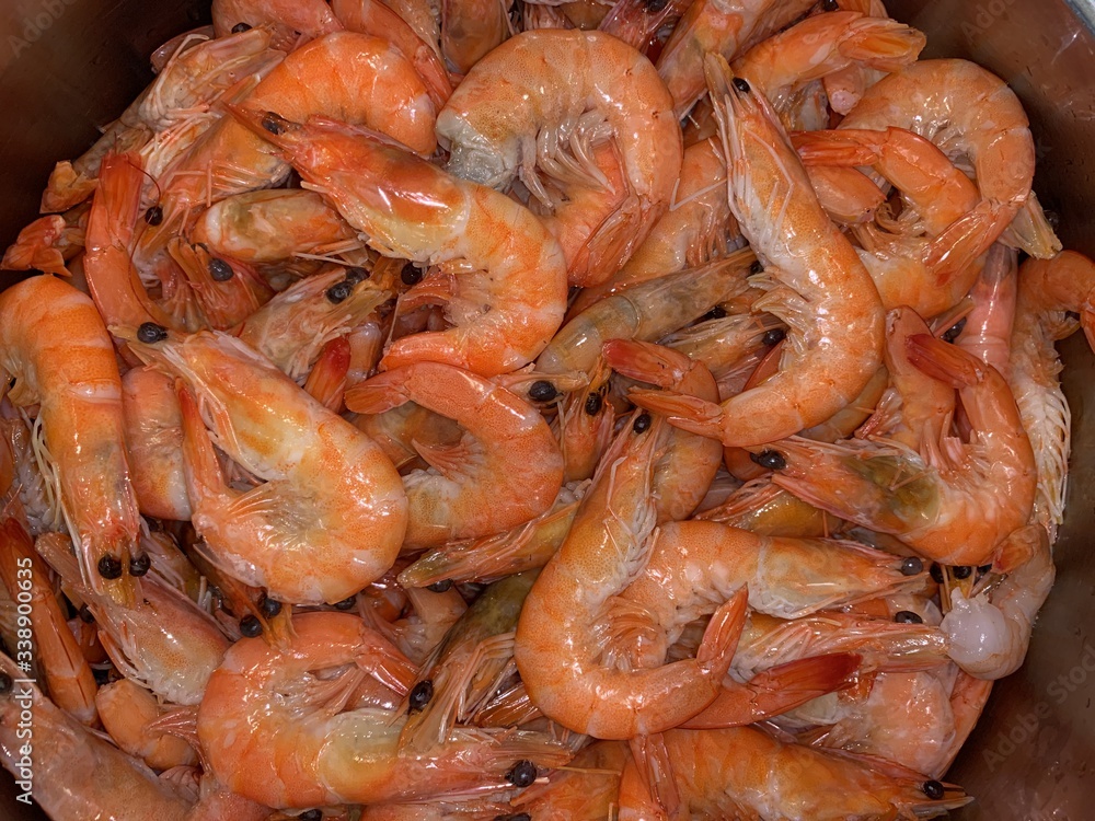 Boiled shrimp in a metal bowl. A large pink shrimp lies on a plate.
