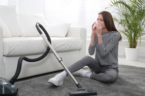 Young woman suffering from dust allergy while vacuuming house