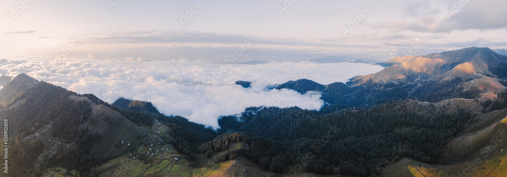 Beautiful panorama view to sunny mountains in Georgia. Bahmaro village location, near Svaneti region. Aerial shot above the clouds. Green hiils and big valley on the horizon. True nature.