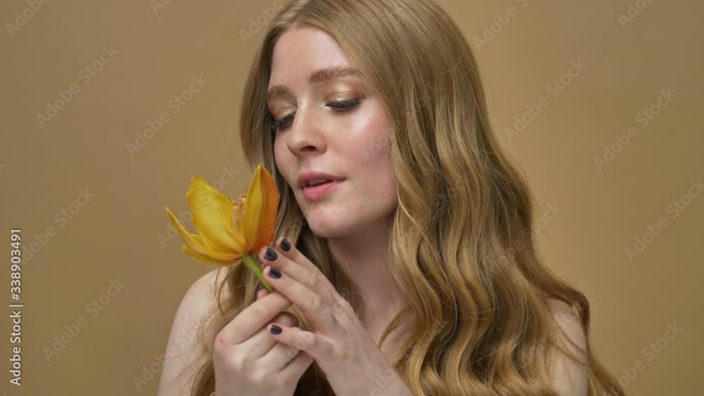 A pleased gorgeous young half-naked woman with long hair is holding a beautiful flower isolated over beige background A pleased gorgeous young half-naked woman with long hair is holding a beautiful flower isolated over beige background