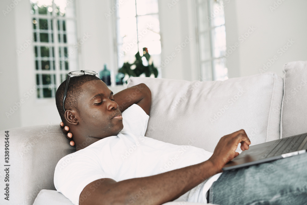 A man of African appearance at home in front of a laptop on a sofa resting A man of African appearance at home in front of a laptop on a sofa resting