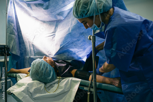 Anesthetist applying blood pressure cuff to patient in operating room photo