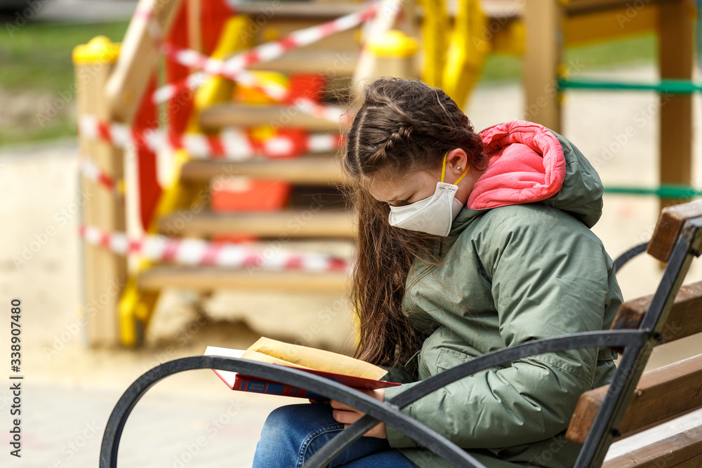 Obraz premium A masked teenage girl is reading a book in the playground.