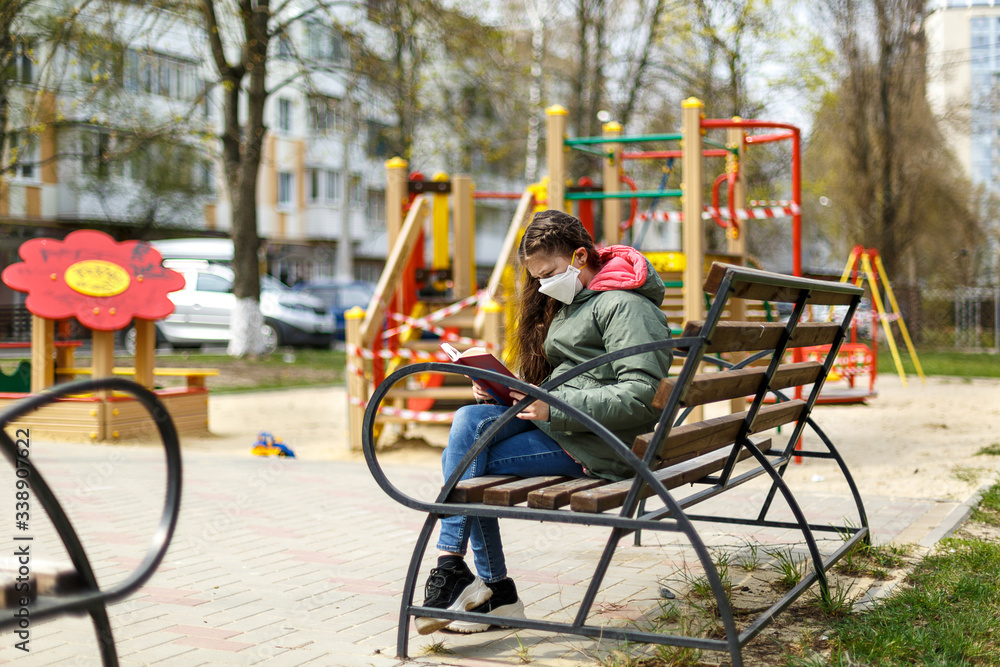 A masked teenage girl is reading a book in the playground. A masked teenage girl is reading a book in the playground.