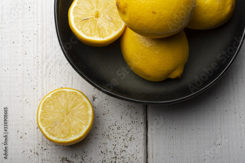 Yellow lemons in a black bowl, on a white wooden table.
