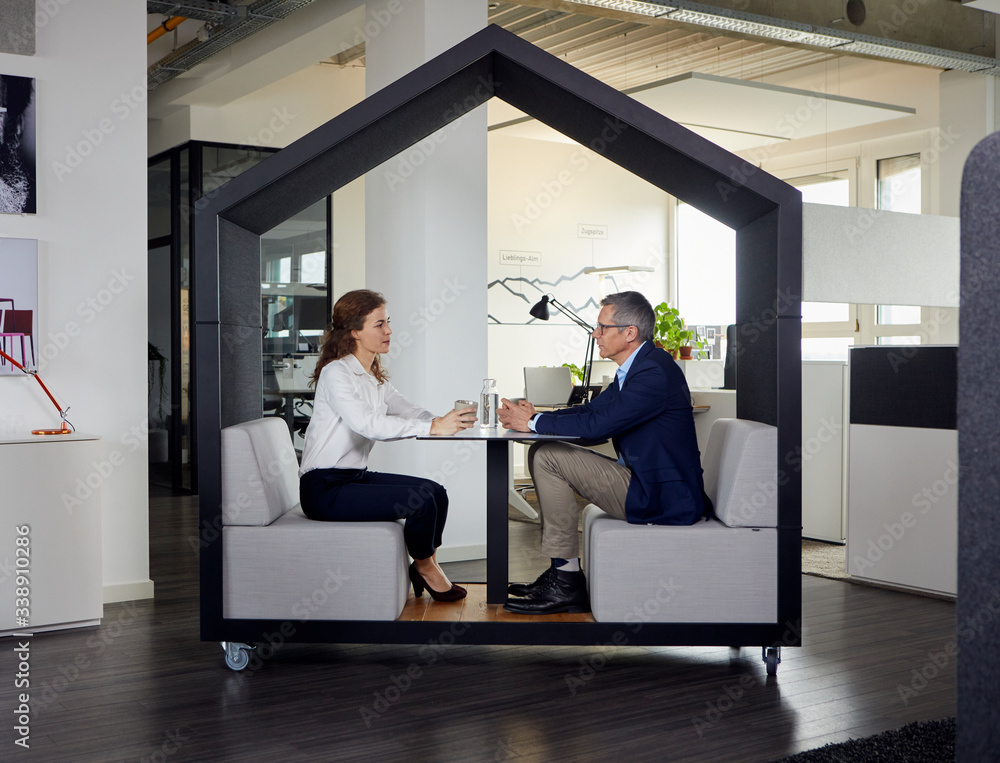 Businessman and businesswoman sitting in a wheeled cubicle in office Businessman and businesswoman sitting in a wheeled cubicle in office