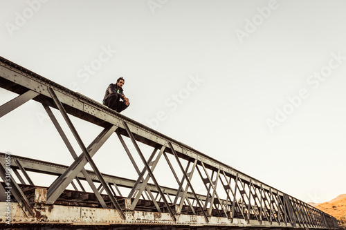 Man crouching on metal bar of an old railway bridge