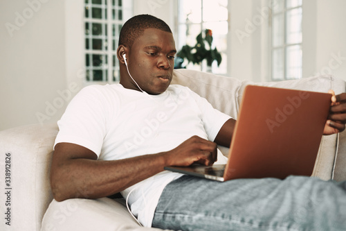 A man of African appearance at home in front of a laptop communicating with headphones