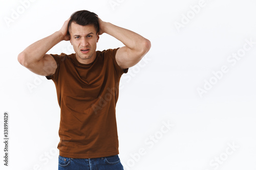 Portrait of distressed and upset, gloomy handsome man hold hands on head and sighing, express disappointment, let down, losing and having bad day, standing upset over white background © Cookie Studio