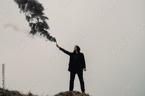 A man stands on a mountain with a smoke bomb in his hand.
