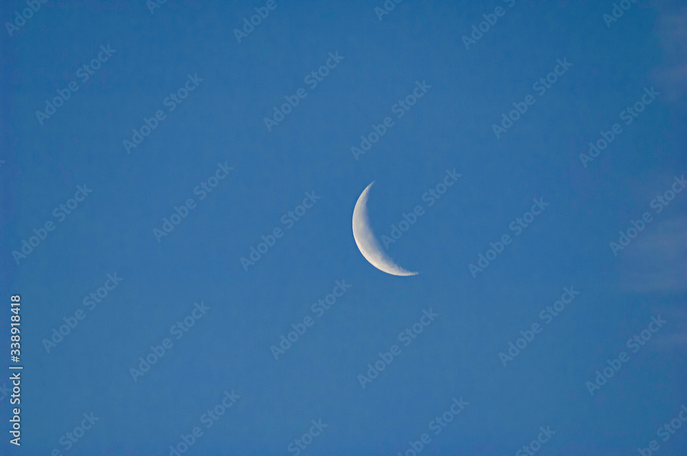 A slim sliver of the silvery moon set on an expanse of a partly cloudy blue sky. A slim sliver of the silvery moon set on an expanse of a partly cloudy blue sky.