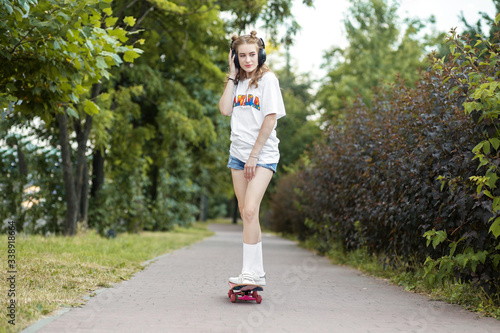 Fototapeta Naklejka Na Ścianę i Meble -  Teen girl rides on a skateboard. Listens to music on headphones. The concept of an hobby, music and sport.