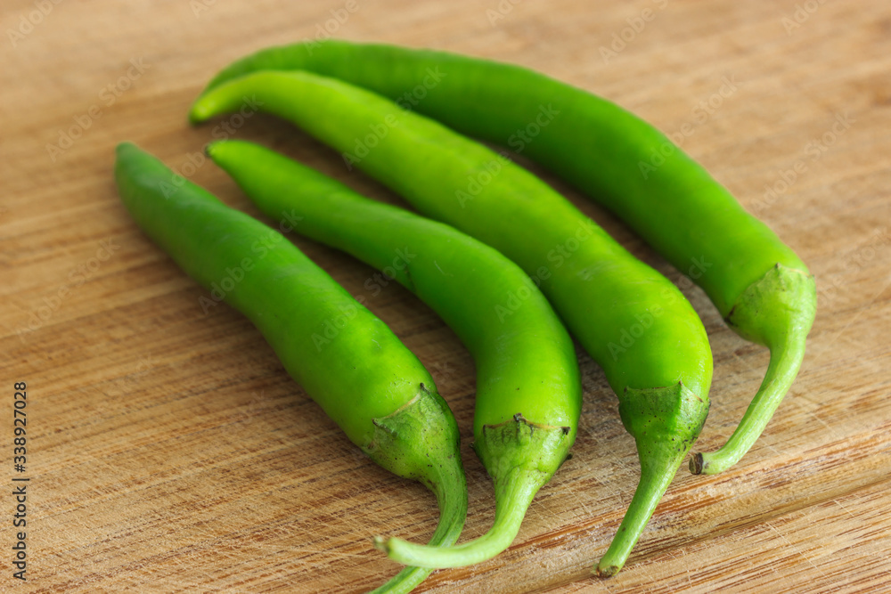 Four green peppers on the wooden chopping board at kitchen. Close-up photo of peppers. Four green peppers on the wooden chopping board at kitchen. Close-up photo of peppers.
