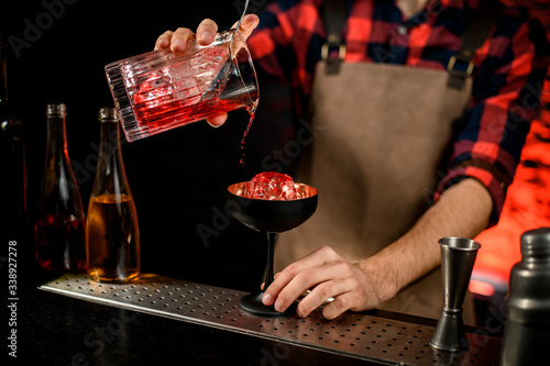 Male bartender accurate pours red campari drink from mixing cup to wineglass