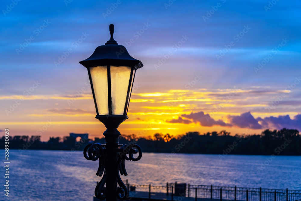 Ancient street lamp against the background of the river at sunset time