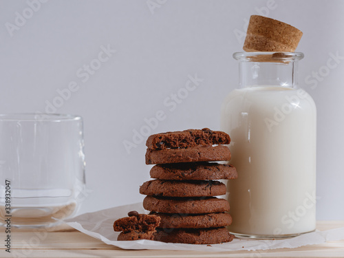 Chocolate cookies with chocolate chips and bottle of milk on white background.