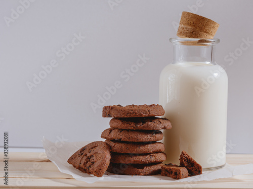 Chocolate cookies with chocolate chips and bottle of milk on white background.