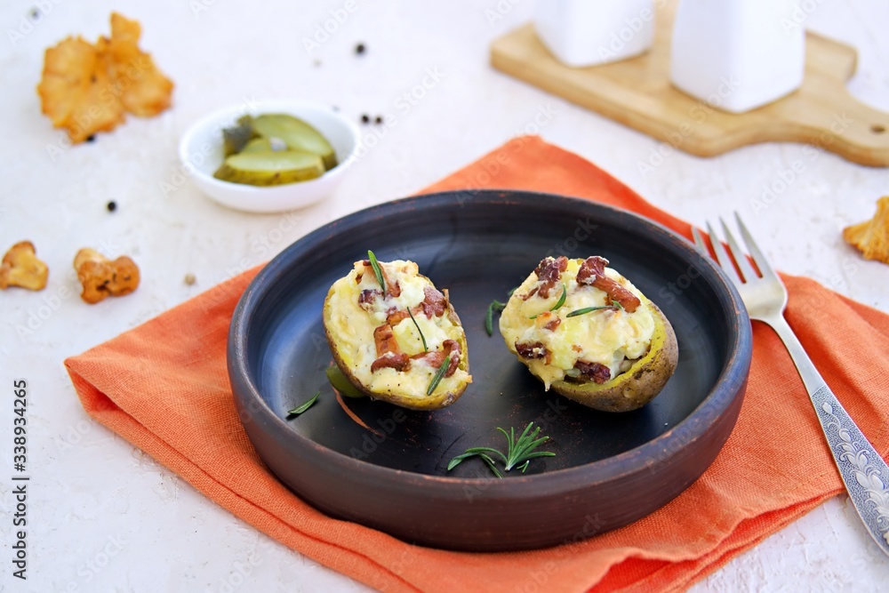 Twice baked potatoes with cheese and chanterelle mushrooms on a brown clay plate on a light concrete background. Recipes with potatoes. Cooking wild mushrooms. Twice baked potatoes with cheese and chanterelle mushrooms on a brown clay plate on a light concrete background. Recipes with potatoes. Cooking wild mushrooms.
