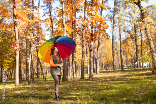 Bilde på lerret Beautiful young girl with long hair in a trouser suit with a rainbow umbrella walks through the autumn park