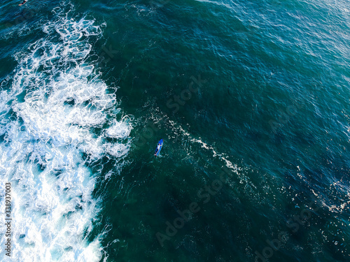 The surfer moving around on surfboard in the tropical blue ocean on the popular surf spot trying to catch a wave. Top view aerial drone landscape, Bali, Indonesia.