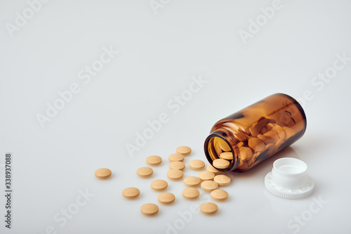 Yellow round tablets scattered from a small brown glass bottle laying on white acrylic table next to white plastic lid