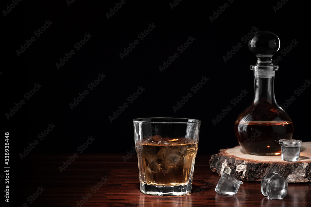 Crystal decanter or carafe of whiskey on cross section of birch tree trunk and glass with alcoholic drink and ice on wooden table in restaurant. Black background for copy space Crystal decanter or carafe of whiskey on cross section of birch tree trunk and glass with alcoholic drink and ice on wooden table in restaurant. Black background for copy space