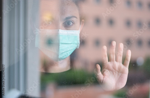 close-up portrait of a woman with a mask behind a window facing the camera