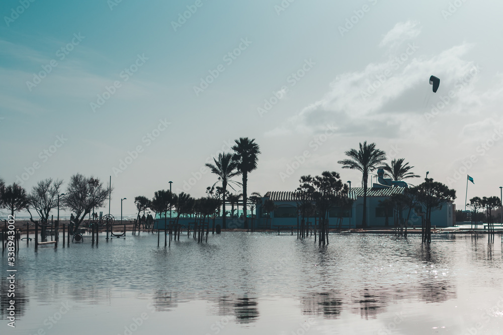 Beach cafe and palm trees in water with reflection after storm that caused flooding. Natural disaster concept