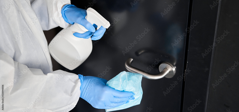 Disinfection, cleaning and washing of door handles. COVID-19. Prevention of coronavirus infection. A woman in a protective suit and blue gloves sprays a disinfectant solution. Prevention of - obrazy, fototapety, plakaty 