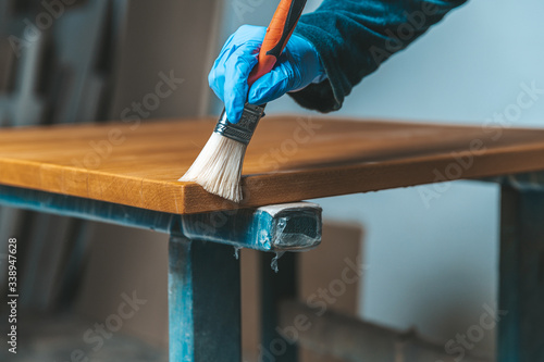 coating of wooden surface with protective varnish. hand in blue rubber glove uses brush
