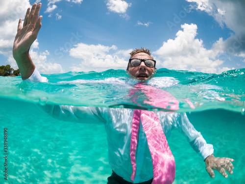 Over-under view of businessman holding his hand up to call for help trying to keep afloat in clear turquoise waters photo
