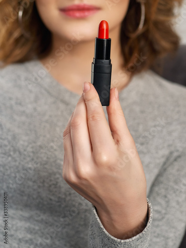 Woman's beauty blogger hands holding professional hi-end red lipstick with blurred body background, warm cozy tones and copyspace