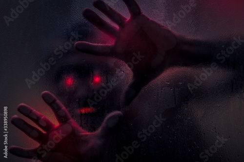 Horror scene of a man with bloody hand against wet shower glass. Toned image. Horror concept