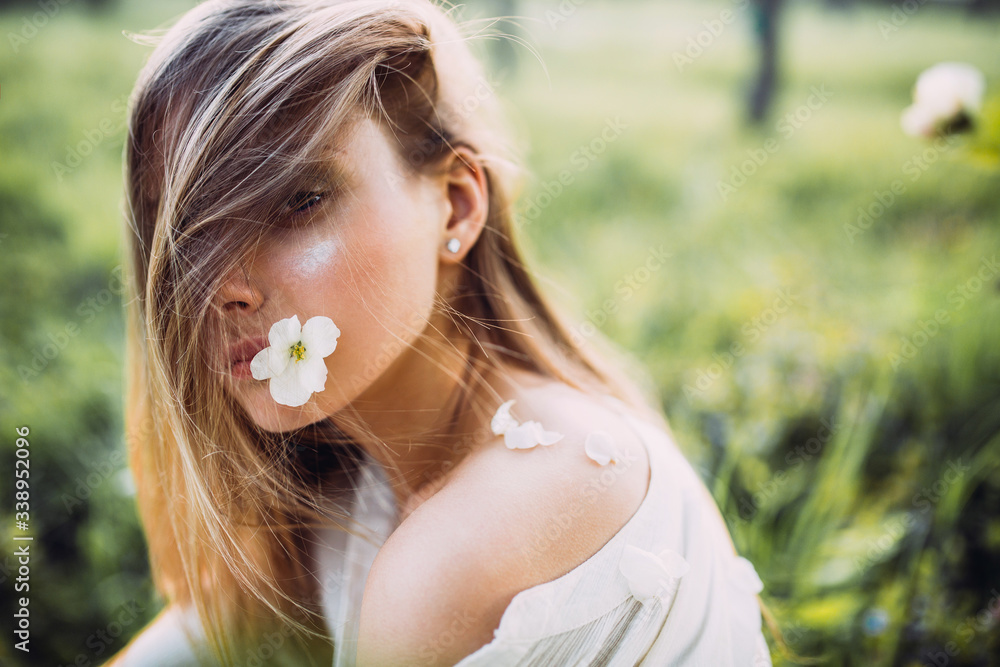 Portrait of a beautiful blonde young woman on a spring day, holding in mouth a white flower of a cherry tree. Portrait of a beautiful blonde young woman on a spring day, holding in mouth a white flower of a cherry tree.