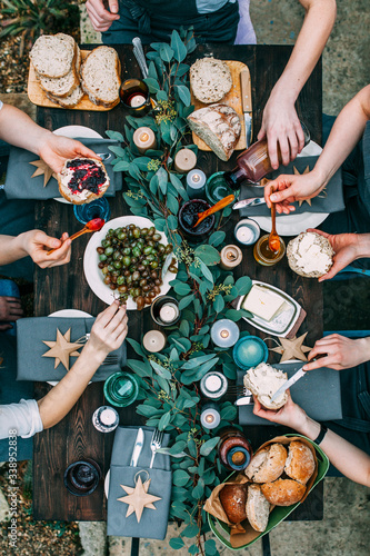 Top view over a dining table, decorated with eucalyptus leaves, with tableware and food. Backyard picnic with friends or neighbors. 