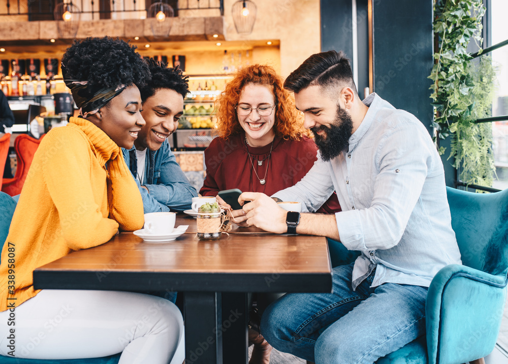 © Sanja - Four friends looking at the phone in a cafe.