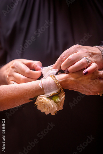 Mother tying a tulle wrist band with roses on her daughter's arm for her wedding ceremony photo