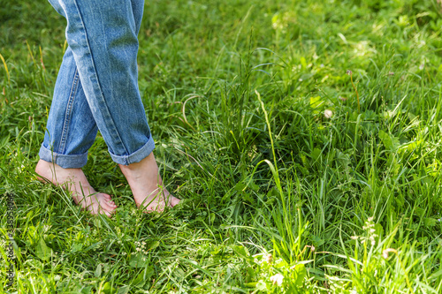 Two beautiful female feet walking on grass in sunny summer morning. Light step barefoot girl legs on soft spring lawn in garden or park. Healthy freedom relax concept.
