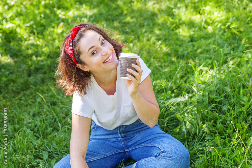 Happy girl smiling outdoor having lunch break. Beautiful young brunete woman with take away coffee cup resting on park or garden green grass background. Education freelancer resting leisure concept. Happy girl smiling outdoor having lunch break. Beautiful young brunete woman with take away coffee cup resting on park or garden green grass background. Education freelancer resting leisure concept.
