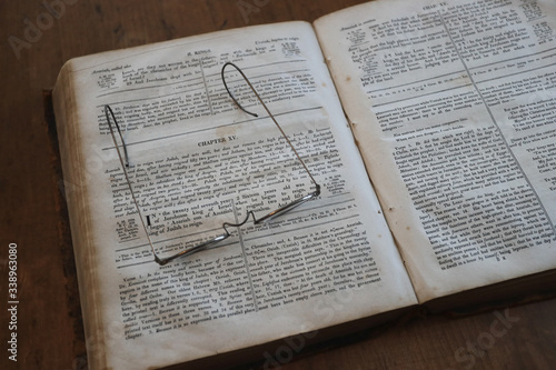 Fotografi Old Bible open with antique reading glasses
