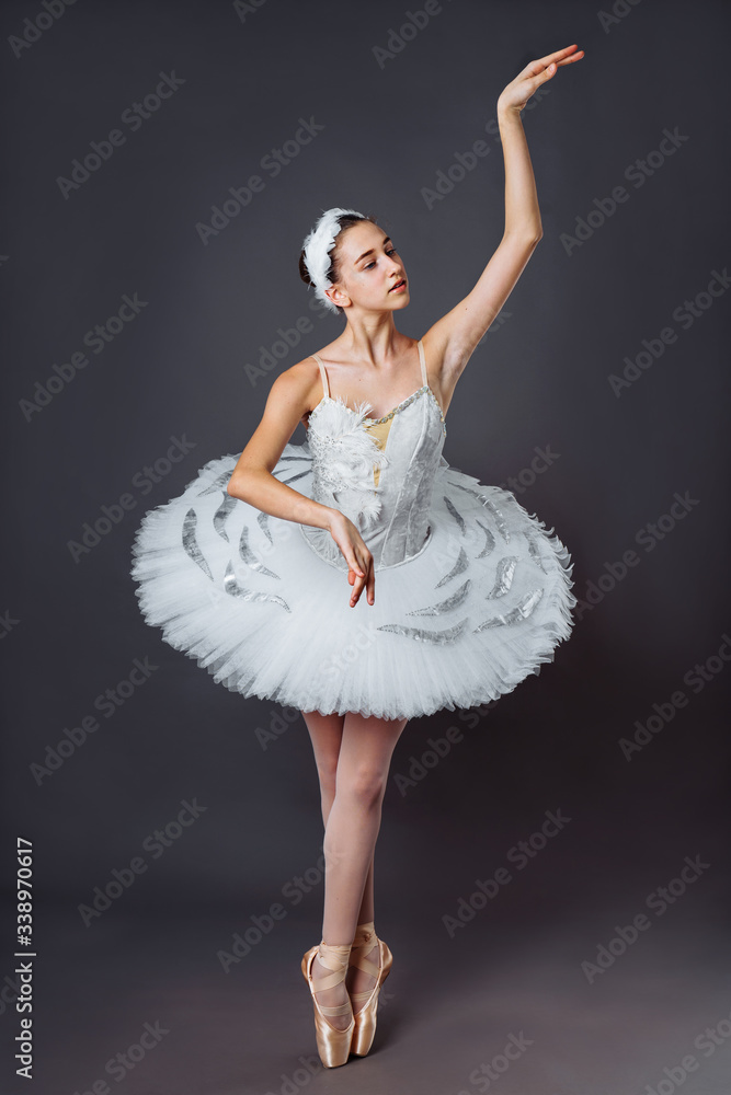 Naklejka premium Ballerina dancing in white dress. Color photo. Graceful ballet dancer or classic ballerina dancing isolated on grey studio background. Ballerina on point shoes feet tutu from Lake Swan