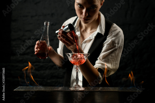 female bartender accurate pours drink into glass which standing on burning bar counter