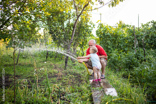 Grandfather with granddaughter in the country water the garden