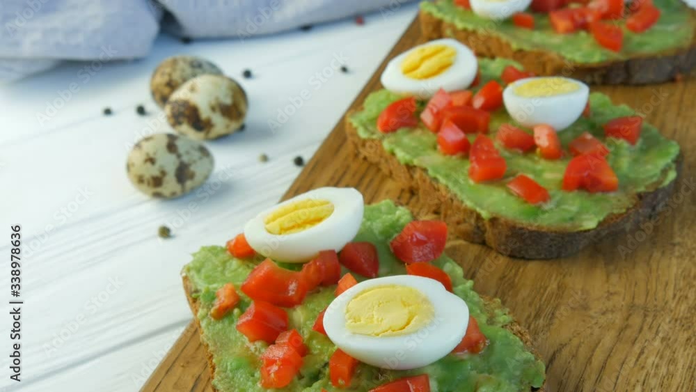 Healthy Vegan food. Spread mashed avocado on a toasted brown bread. Making tasty avocado toast for breakfast. Cooking bruschetta with cherry tomatoes and quail eggs Healthy Vegan food. Spread mashed avocado on a toasted brown bread. Making tasty avocado toast for breakfast. Cooking bruschetta with cherry tomatoes and quail eggs
