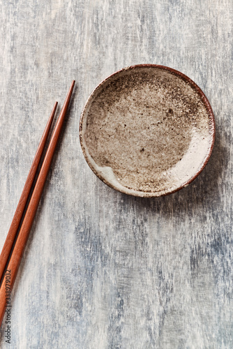 Wooden chopsticks and empty ceramics plate on rustic wooden background. Top view. Copy space.